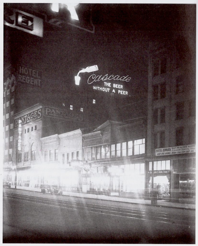 1912 Vancouver street at night with neon signs and theatres.